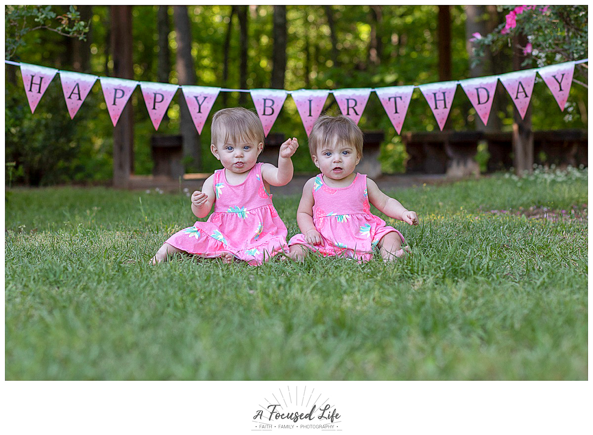 twin girls sitting on the ground with banner