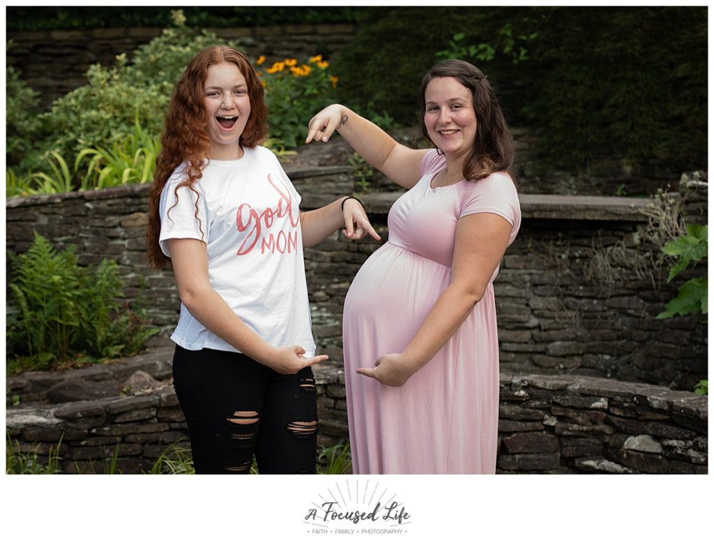 Pregnant mom posing for maternity pictures with sister wearing "God mom" shirt at Vines Park in Loganville