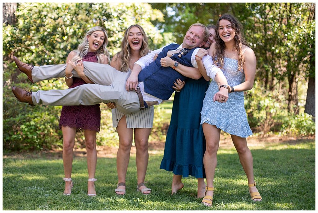 Bridesmaids holding groom in the air and laughing