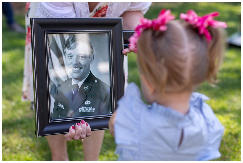 Toddler girl looking at framed picture of passed Grandfather
