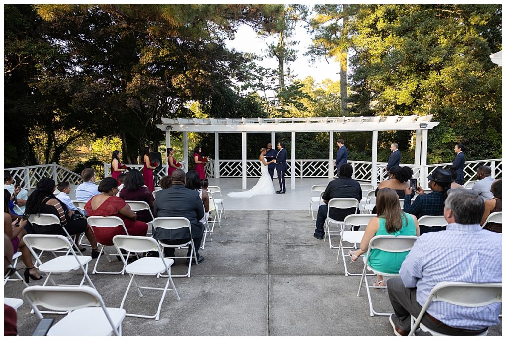 Outdoor ceremony with white chairs and green trees in background at Vines Mansion in Loganville GA