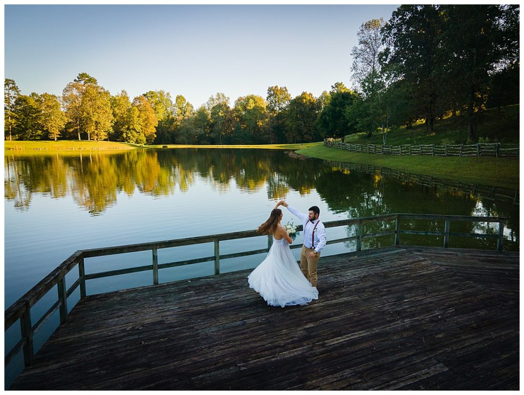 Bride and groom dancing on wooden platform outside with water in the background