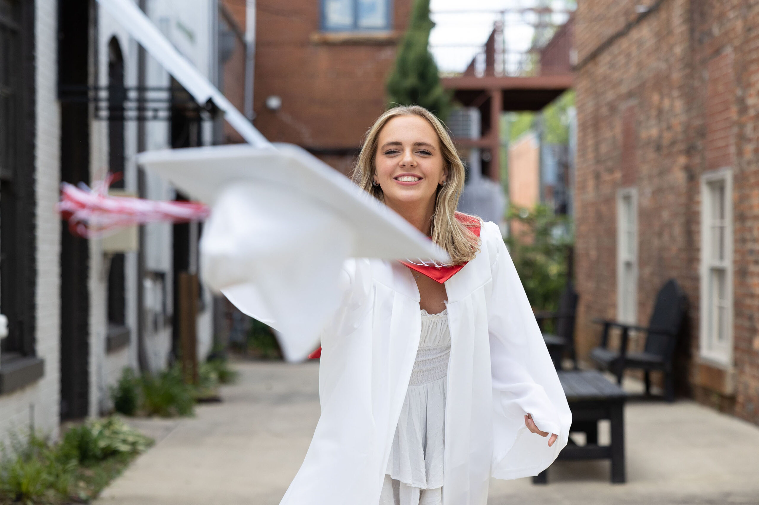 high school senior girl in white graduation gown throwing graduation cap at camera