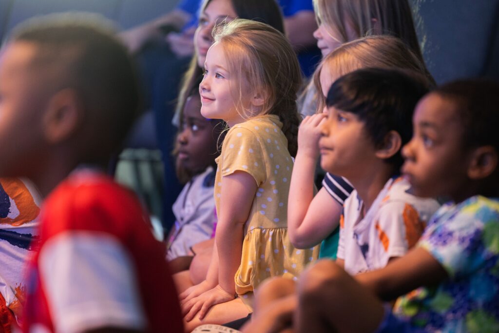 Kids watching a VBS slideshow in the church sanctuary at the screen as their pictures appear.